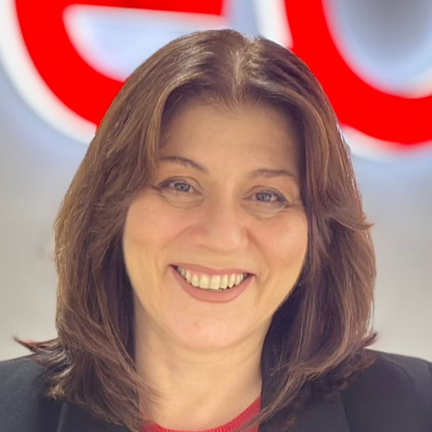 Белен Бареиро, агент за контакт центар во EOS во Шпанија, се потпира на шалтер во црн блејзер пред светлото лого на EOS.