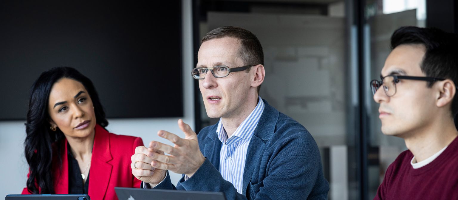 Три лица водат разговор во канцеларија.