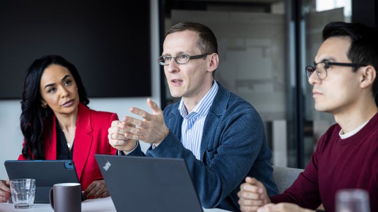 Три лица водат разговор во канцеларија.