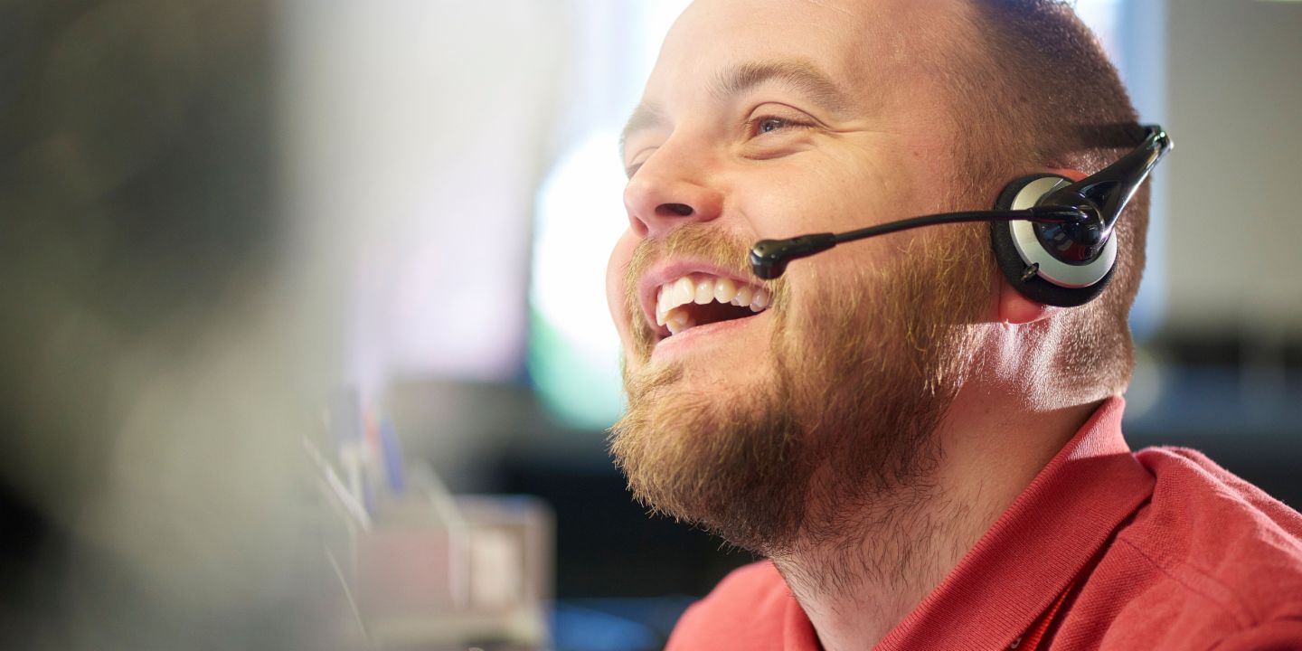 A young man with a headset smiles while on the phone.